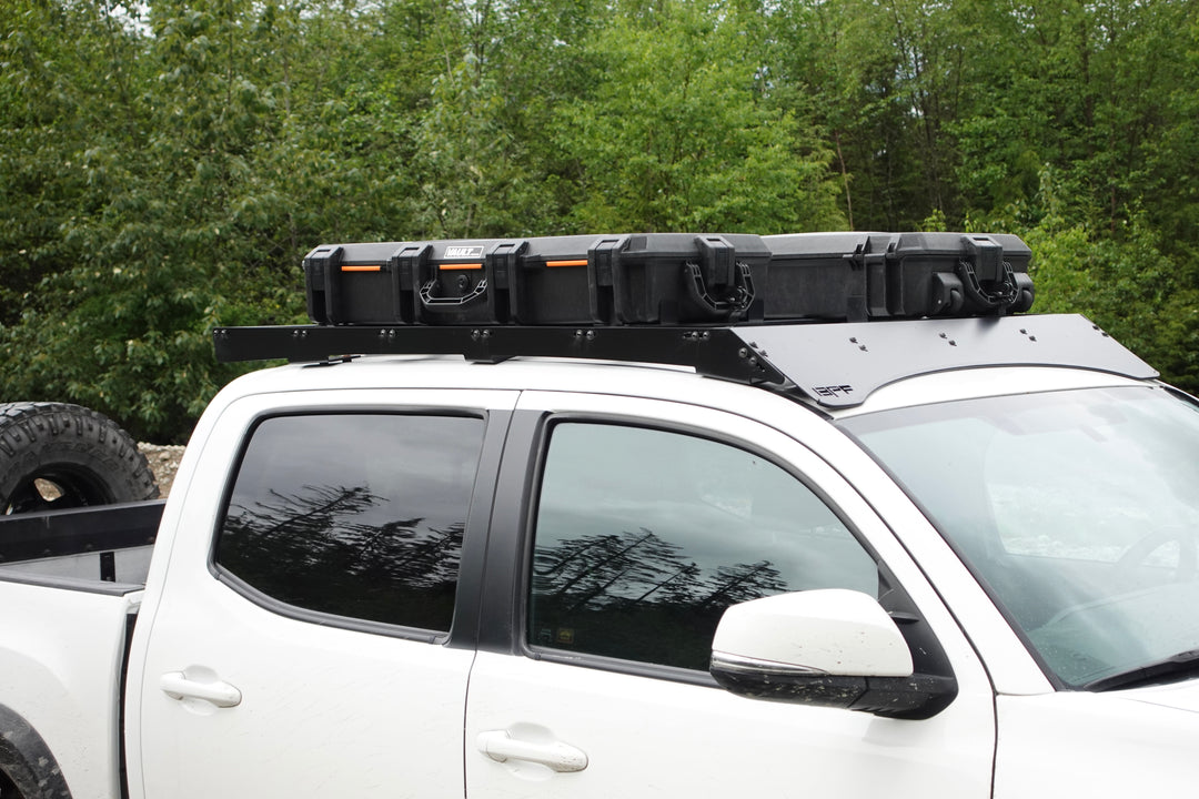 BPF Universal Pelican Vault V700 Case Mounting brackets securely attached to a white truck roof rack, showing durable black case mounted for overlanding gear storage and transport.