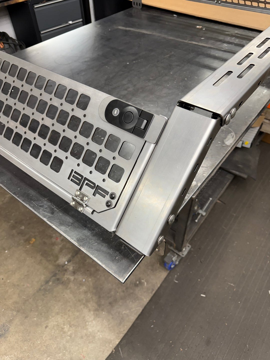 Close-up view of a metallic bed rack corner with perforated grill mesh and lock mechanism, part of the 05-26 Tacoma Bed Rack fits 2nd,3rd and 4th gen Tacomas, designed for secure cargo storage and durability.