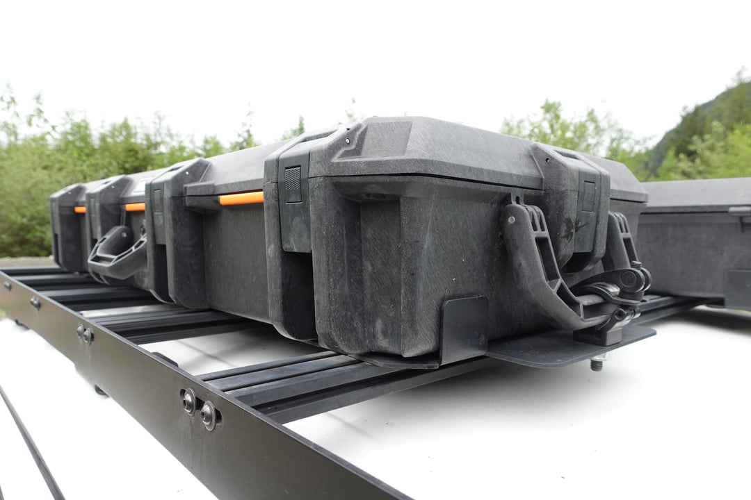 BPF Universal Pelican Vault V800 and V730 Case Mounting brackets securing multiple black protective Pelican Vault cases on a roof rack setup outdoors.