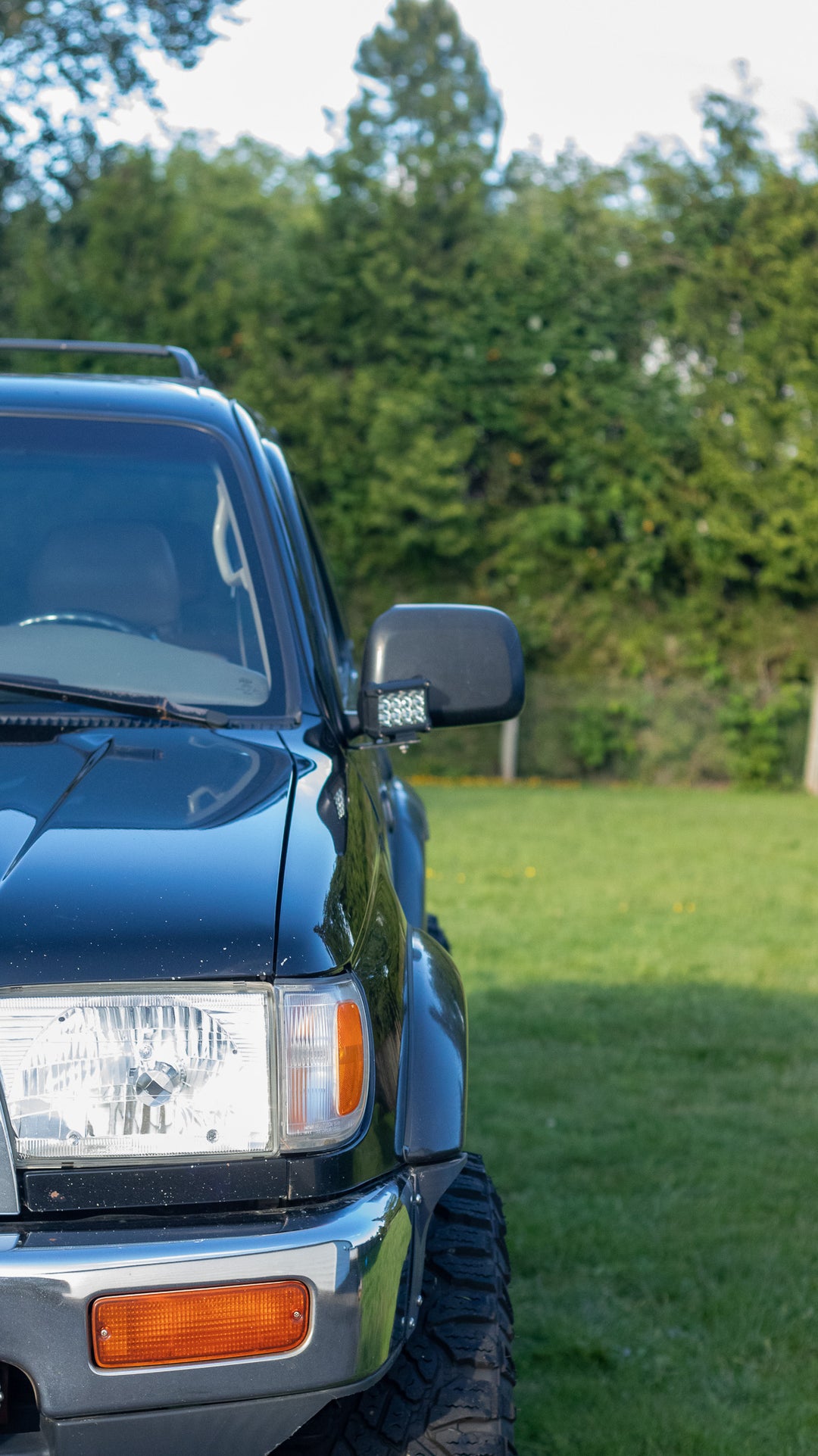 Front view of a dark blue Toyota 4Runner equipped with BPF 1996-2002 Toyota 4Runner Light Brackets mounted near the side mirror on a grassy outdoor background.