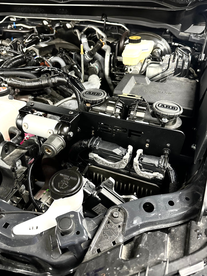 Close-up view of a black BPF 2024-2025 Tacoma and Land Cruiser Twin Compressor Mount securely installed in an engine bay, highlighting its sturdy CNC fabricated design and integrated compressor units.