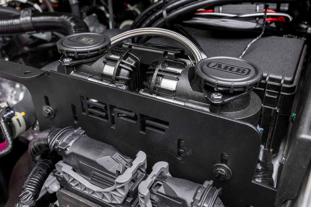 Close-up of a BPF 2025+ 4runner twin compressor mount installed in an engine bay, featuring two ARB compressors secured by a durable black mounting bracket with visible wiring.