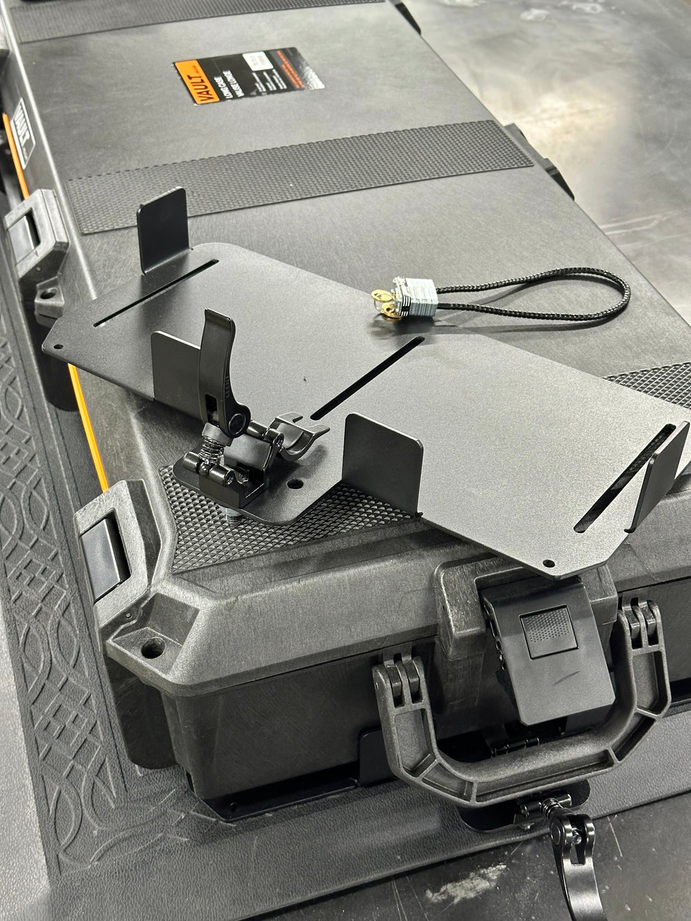 Black powder-coated steel BPF Universal Pelican Vault V700 Case Mounting brackets with adjustable clamp and locking cable, designed for secure heavy-duty case attachment.