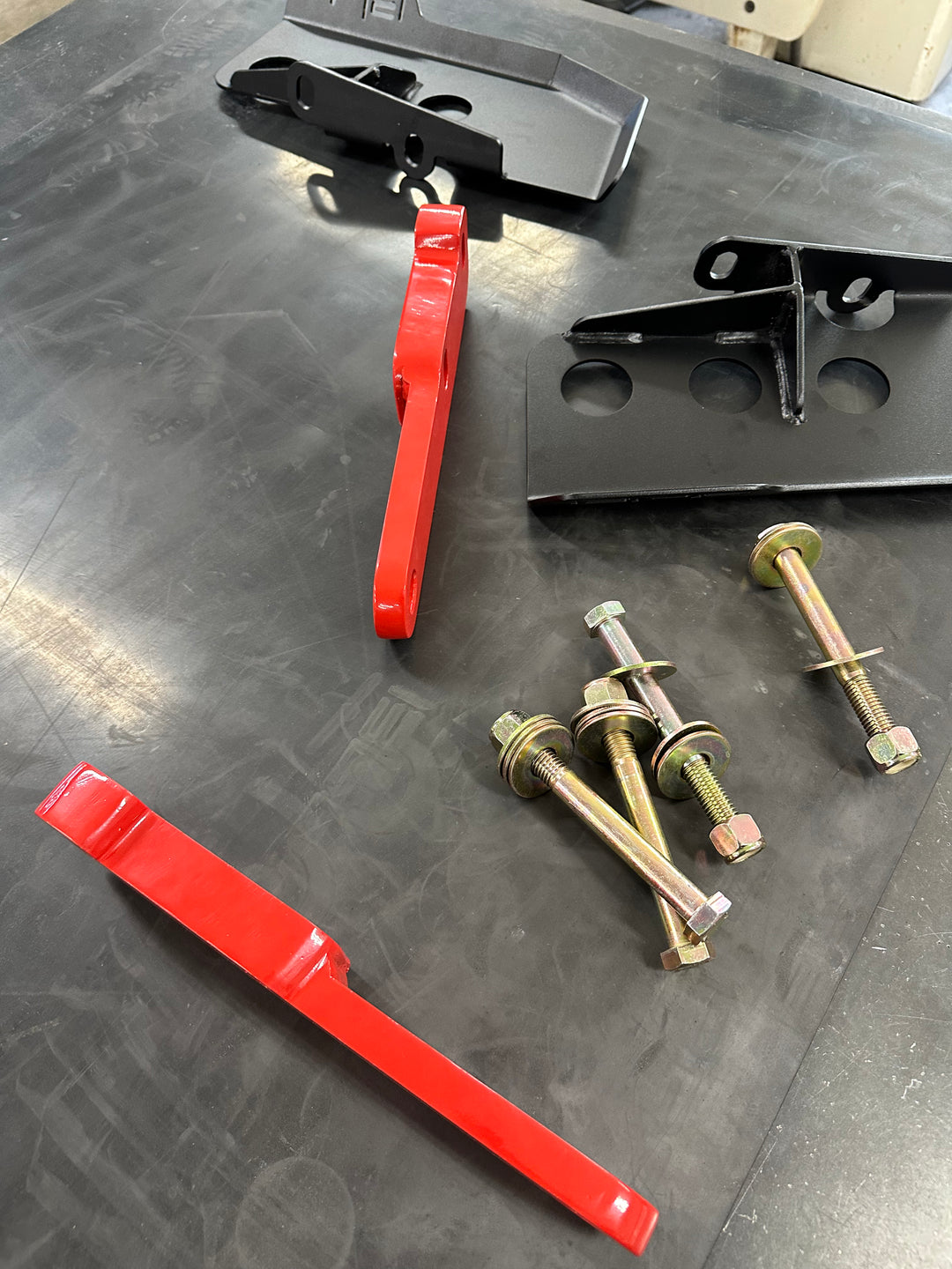 BPF 4th gen Tacoma rear tow hooks with integrated skid plates shown with red hooks, black mounting brackets, and gold hardware on a dark work surface.