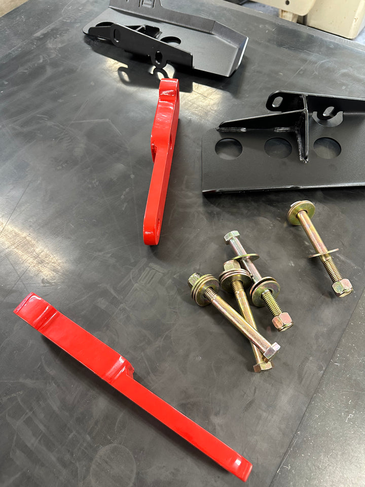 BPF 4th gen Tacoma rear tow hooks with integrated skid plates shown with red hooks, black mounting brackets, and gold hardware on a dark work surface.