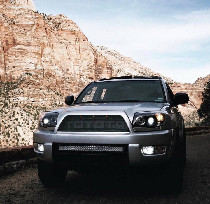 Silver Toyota 4Runner equipped with a BPF 03-09 Toyota 4runner Grill featuring grill mesh and off-road lights, set against a rugged mountain backdrop for overlanding adventures.
