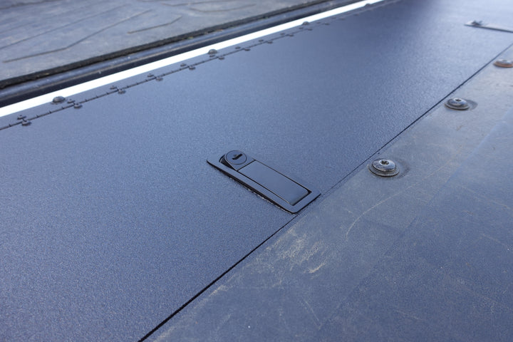Close-up of BPF 2016-2023 Toyota Tacoma Tailgate Panel installed, showing textured black powder-coated surface with secured latch and bolts for OEM fitment and durable protection.