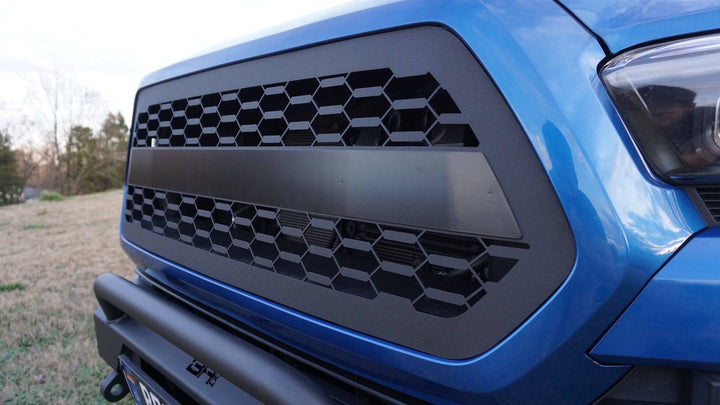 Close-up of a black hexagonal mesh BPF 2016-2023 Toyota Tacoma Grill installed on a blue Toyota Tacoma, showing a durable CNC fabricated design with a sleek powder-coated finish.