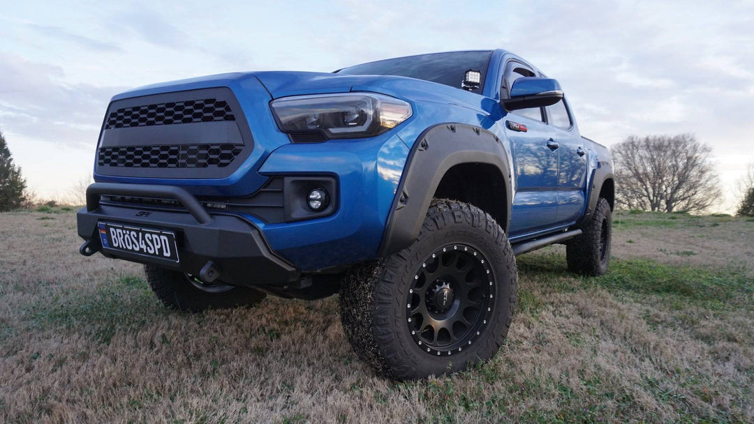 Blue Toyota Tacoma equipped with BPF 2016-2023 Toyota Tacoma Grill featuring black mesh design and rugged off-road tires in an outdoor setting