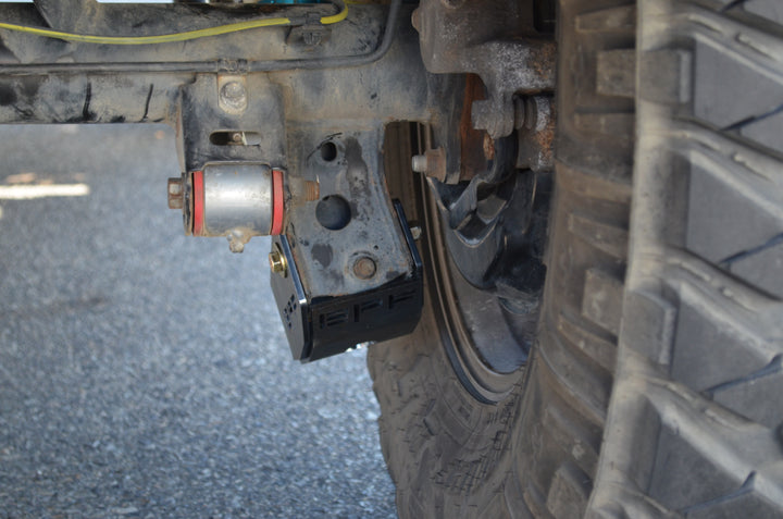 BPF 4runner 04-24/FJ 07-14 Shock Guards installed behind a rugged off-road tire, showcasing durable metal construction and protective design for suspension components.