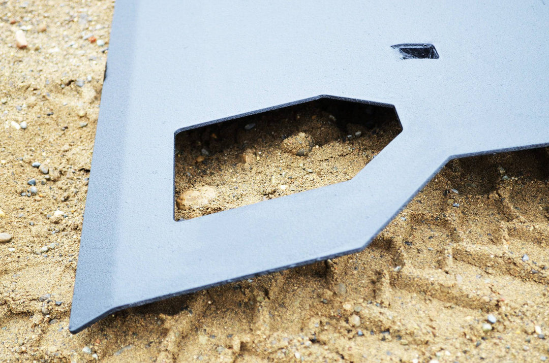 Close-up view of a powder-coated steel skid plate designed for durability and protection, identified as BPF 2005-2015 Toyota Tacoma Skid Plate, resting on sandy terrain.