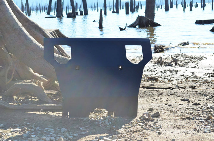 BPF 2005-2015 Toyota Tacoma Skid Plate resting on rocky ground near a lake with tree stumps in the background, showcasing its durable and protective design.