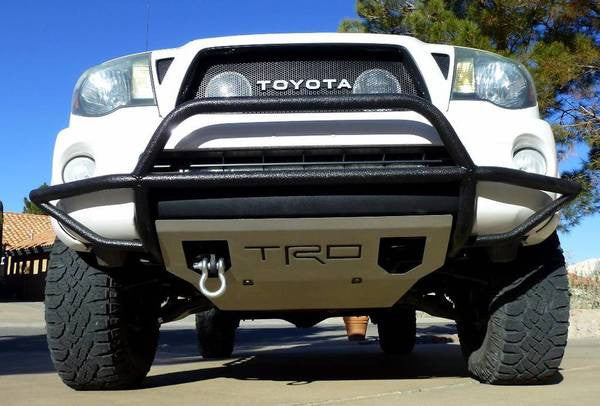 Front view of a white Toyota Tacoma featuring a black heavy duty BPF 2005-2023 HD Tacoma Recovery Tow Hook Passenger Side attached to the front bumper with off-road tires and a protective skid plate.