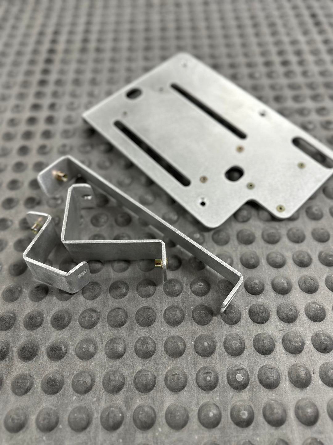 Close-up of CNC fabricated metal components on textured surface, designed for BPF 80 series Land cruiser Fuse block mount with precise slots and mounting points.