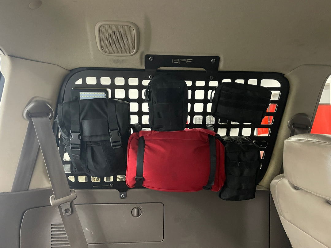 Interior view of a 1990-1997 Toyota Land Cruiser with BPF 1990-1997 Toyota Land Cruiser Storage Panels installed behind the rear seats, featuring multiple attached black and red MOLLE-compatible storage pouches for organized overlanding gear.