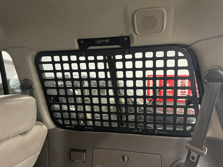 Interior view of a black BPF 1990-1997 Toyota Land Cruiser Storage Panels grid mounted securely behind the rear passenger seat, designed for organized overlanding gear storage and pet barrier use.