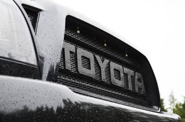 Close-up of a black grill mesh with the large word TOYOTA and installed BPF Grill LED's above the lettering on a wet vehicle surface.
