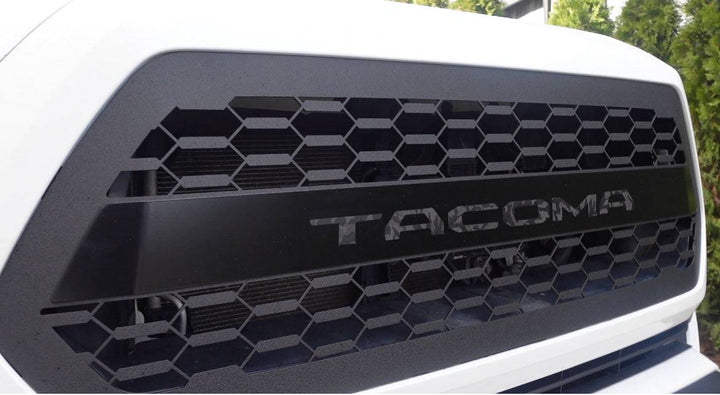 BPF 2016-2023 Toyota Tacoma Grill featuring a black hexagonal mesh design with bold TACOMA lettering, CNC fabricated for a custom fit and powder coated finish.