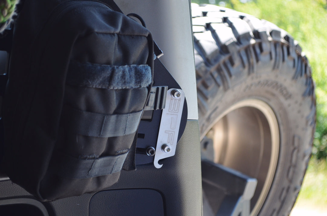 Close-up of a black storage bag attached to BPF 2010-2024 4Runner Storage Panels mounted inside a vehicle near a rugged off-road tire, highlighting durable CNC fabricated metal mounting hardware.