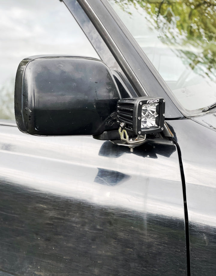 Black side mirror on an off-road vehicle fitted with a mounted auxiliary light using BPF 80 Series Land Cruiser and LX450 Mirror Light Brackets for secure attachment.