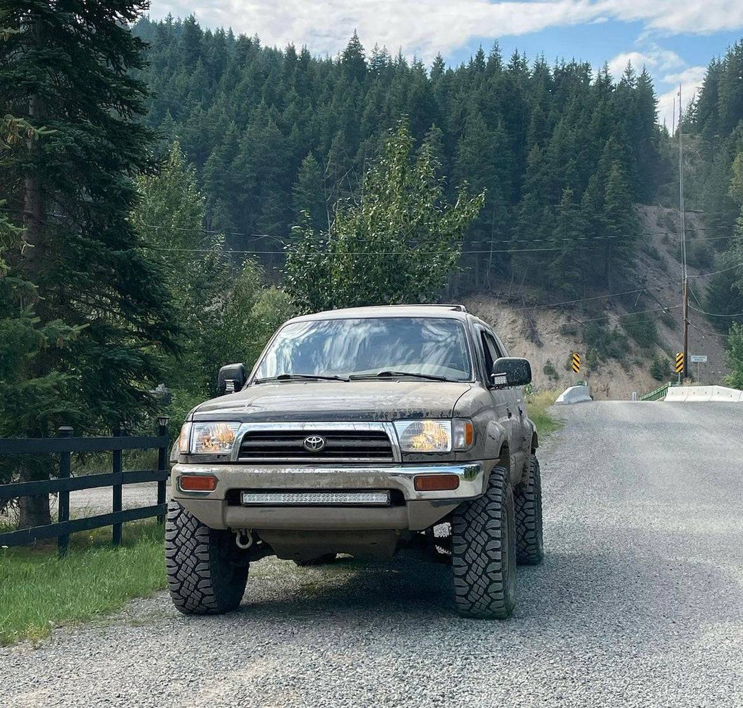 1996-2002 Toyota 4Runner equipped with BPF 1996-2002 Toyota 4Runner Light Brackets, parked on a gravel road surrounded by forested hills under a cloudy sky.