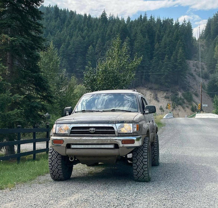 1996-2002 Toyota 4Runner equipped with BPF 1996-2002 Toyota 4Runner Light Brackets, parked on a gravel road surrounded by forested hills under a cloudy sky.